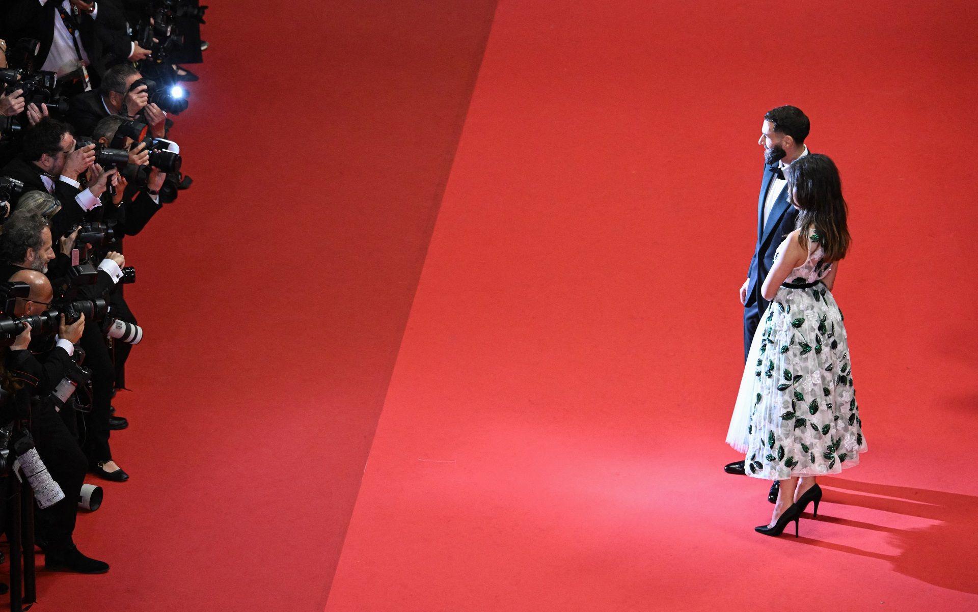 A man and a woman pose for photographers as they walk down a red carpet.