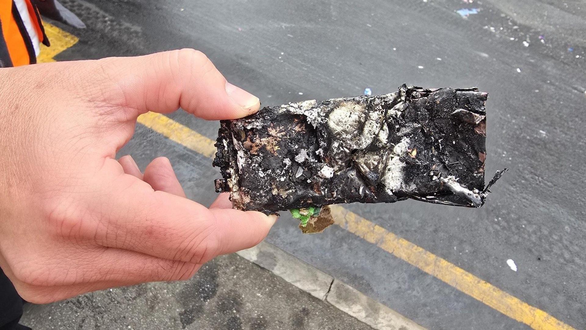 A close up image of a hand holding a badly burnt rectangular object roughly 10cms long and 3cms wide