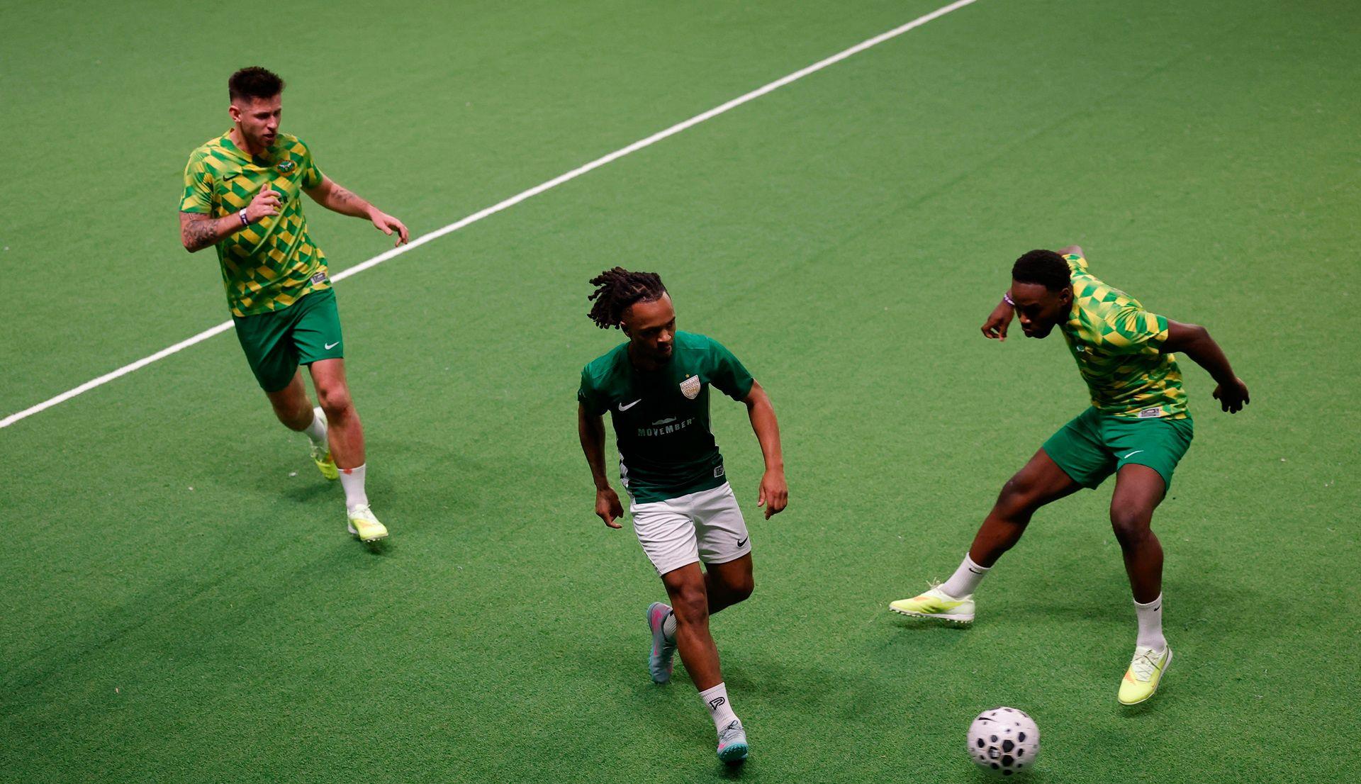 Three people run after a football 