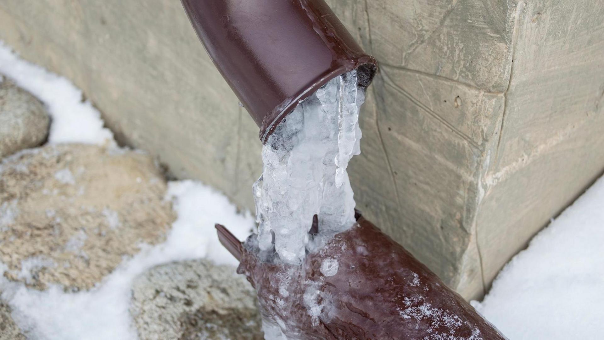 A cracked leaking pipe is frozen inside and out as snow lies on the ground.