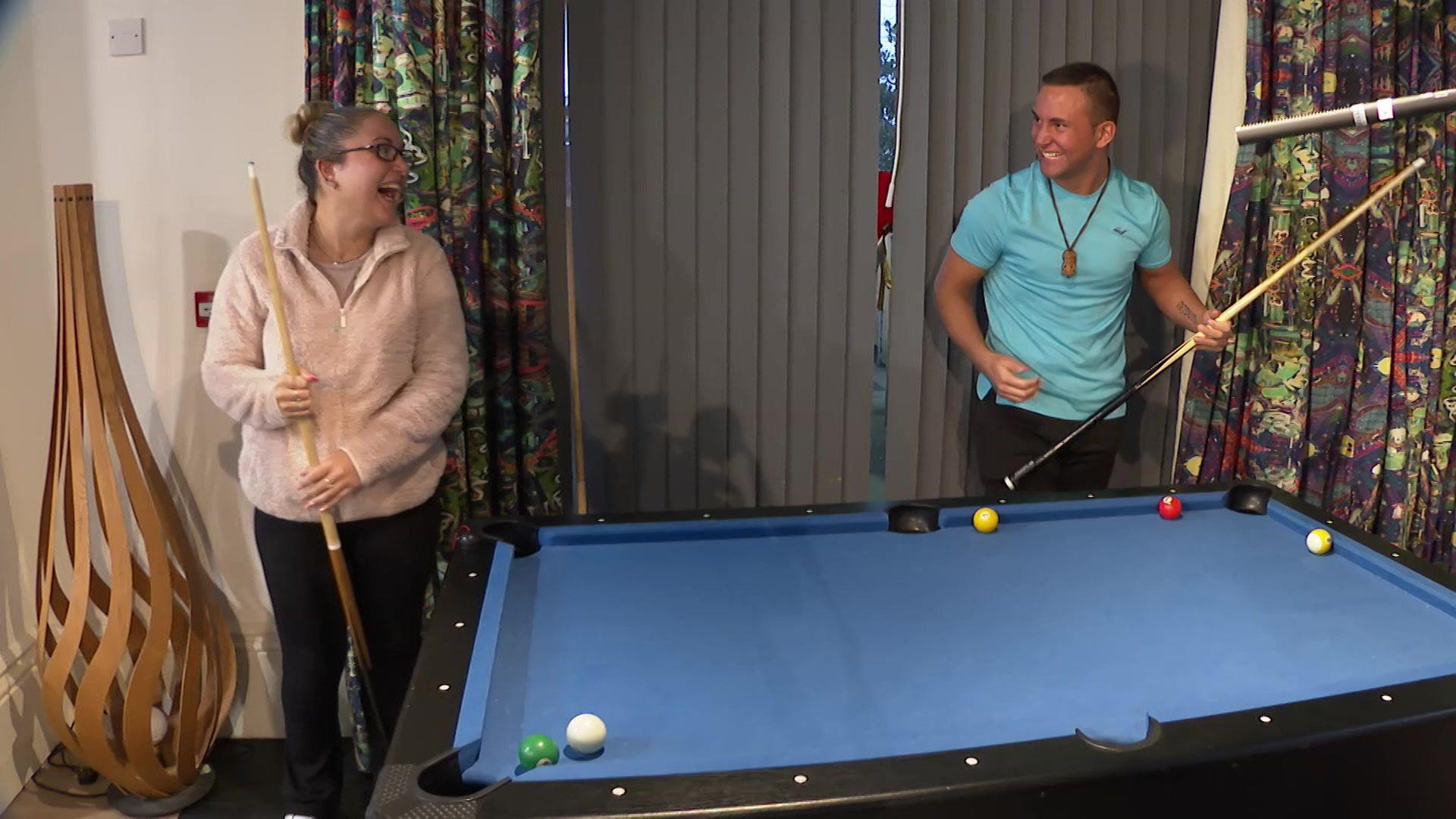 A young woman and a young man laugh together as they enjoy a game of pool.