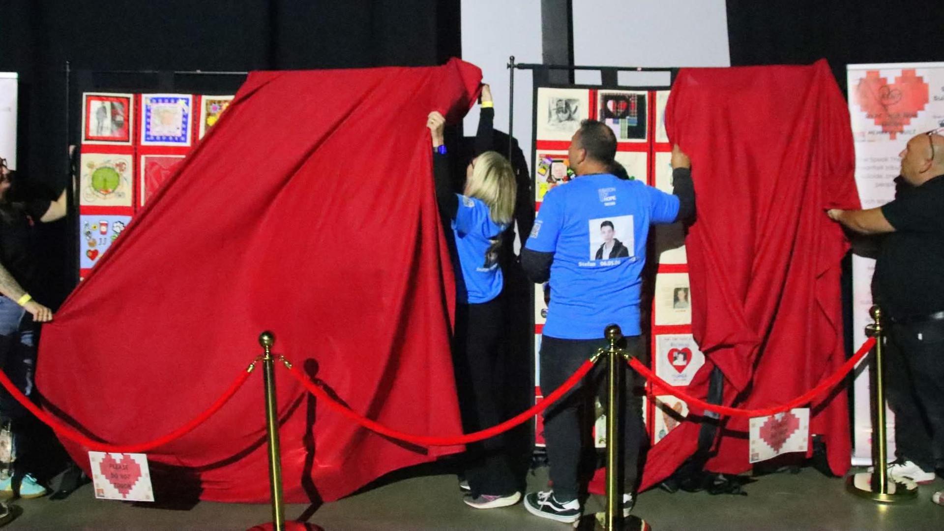 A red curtain being pulled down unveiling the Kent Speak Their Name memorial quilt in Margate