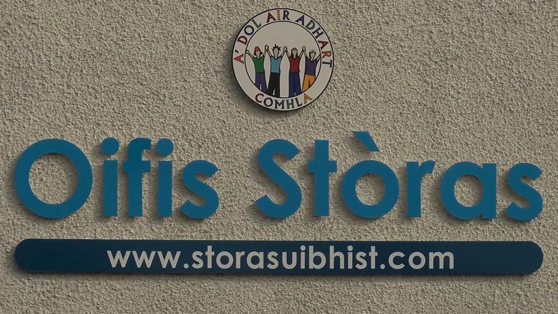 Soidhne air balla ag ràdh Oifis Stòras Uibhist le suacheantas os a chionn ag ràdh A' Dol air Adhart Còmhla