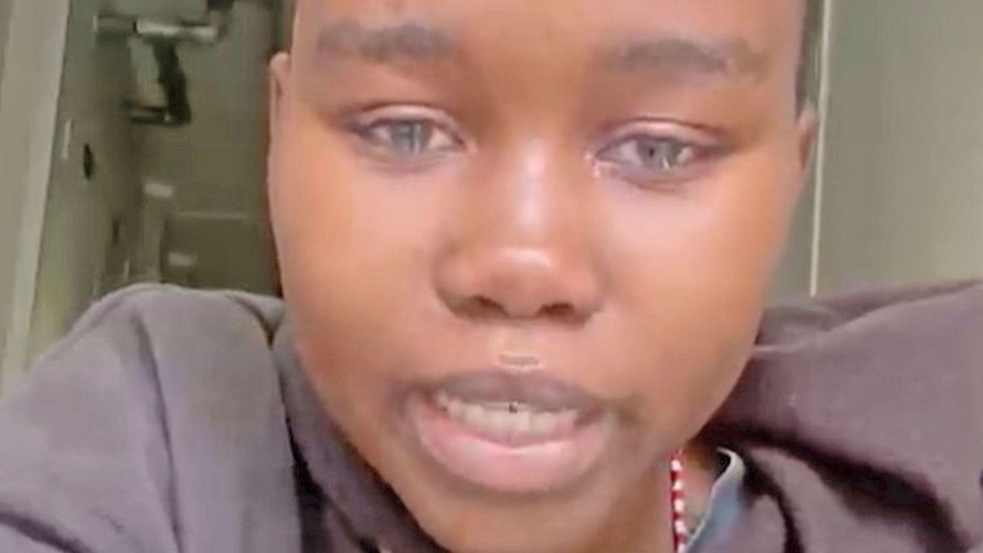 A girl with very short hair looks at the camera crying
