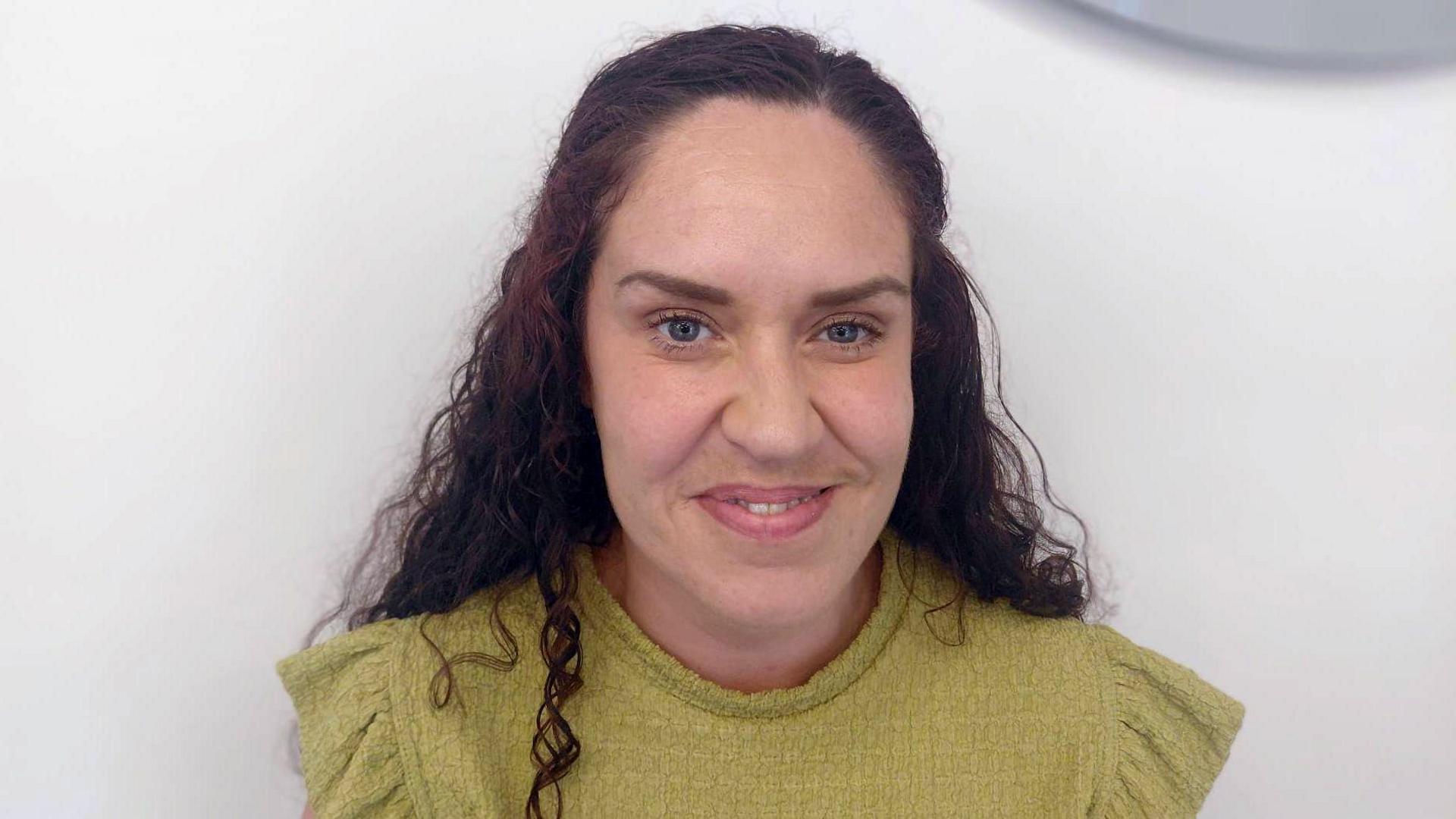 A head and shoulders crop of Carla McLoughlin in a green top smiling while looking into the camera against a grey background.