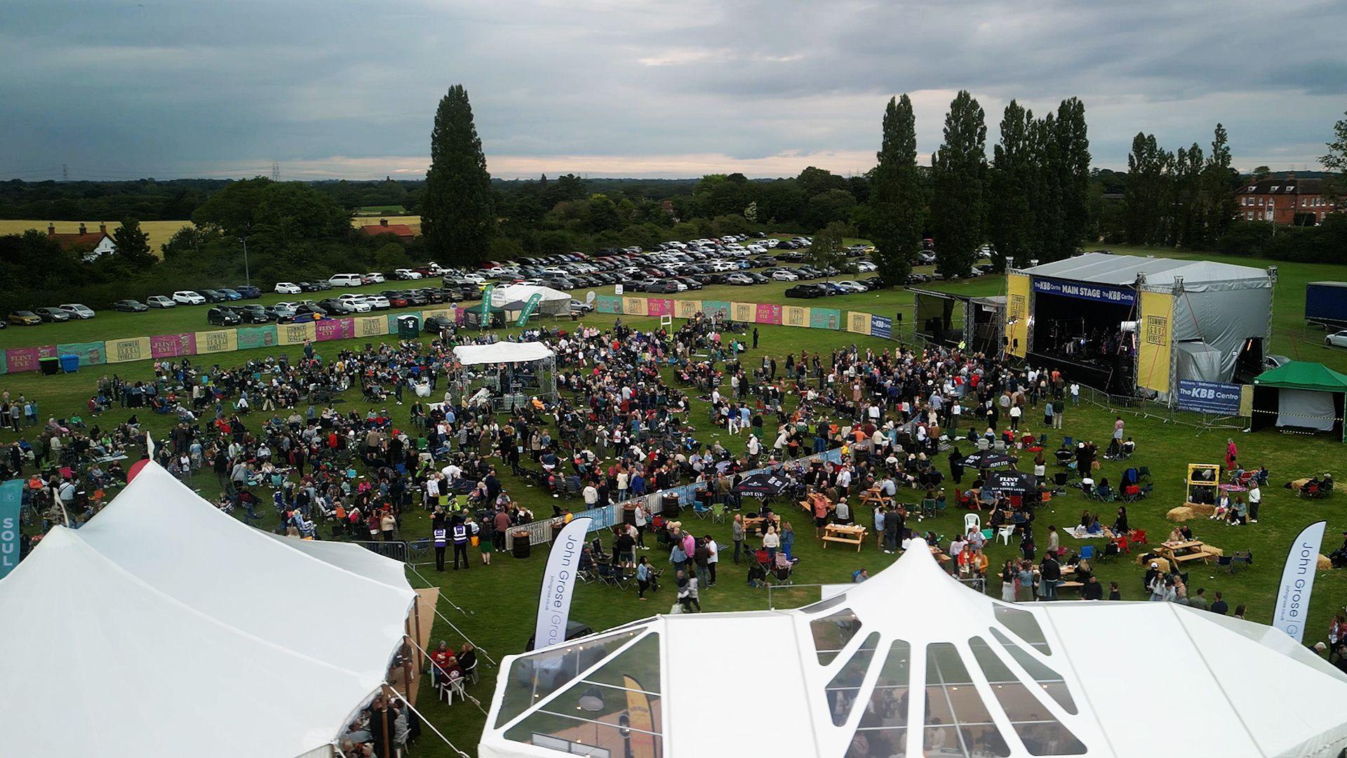 A drone image of Summer Soul Vibes. Attendees are pictured in a large field with a stage at one end. Other tents can be seen dotted around the outside of the venue.