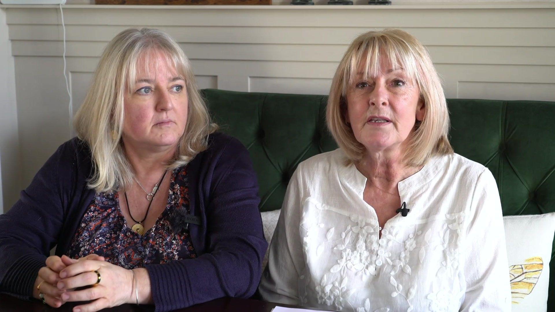 Samantha Griffiths, who has blonde hair and wears a purple cardigan, and Karen Paddock, also blonde with a white blouse, sit on a green couch