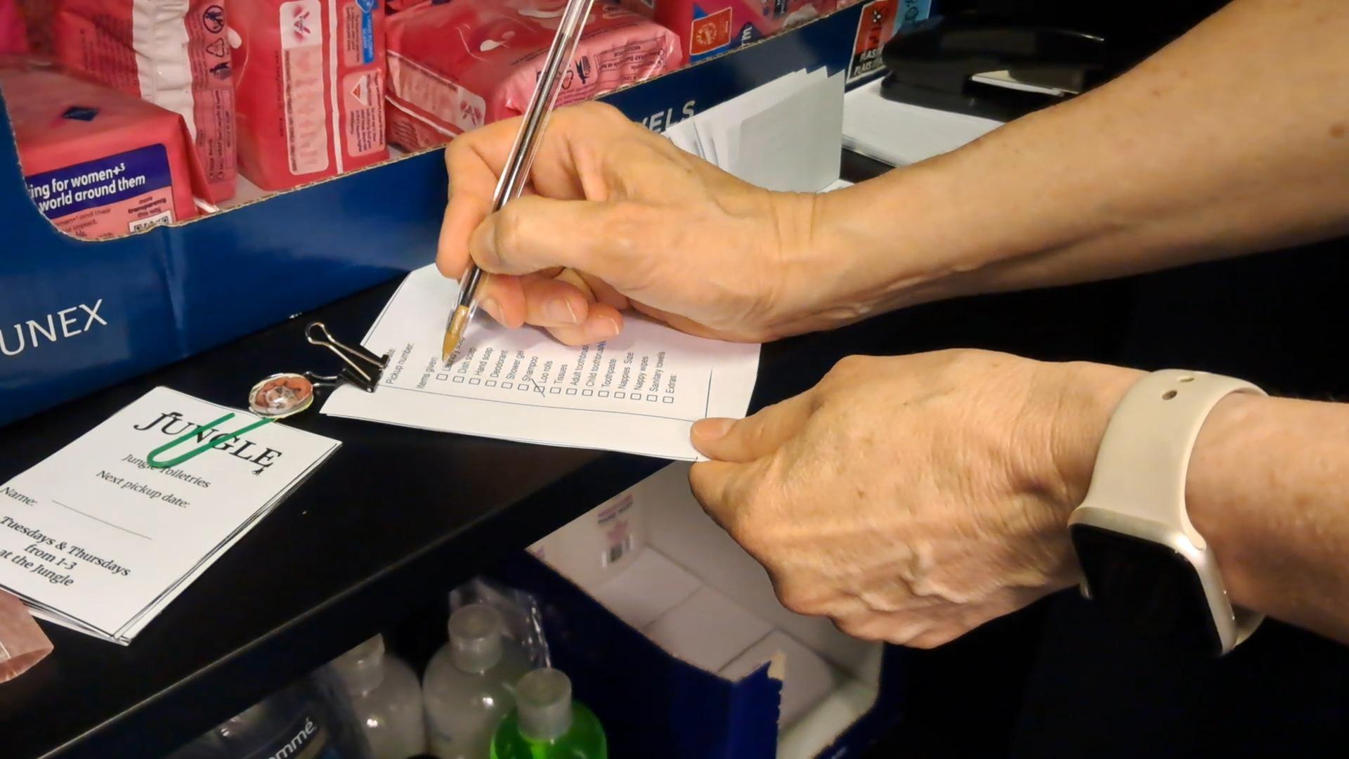 A close-up shot of someone checking off a list of toiletries with a pen.