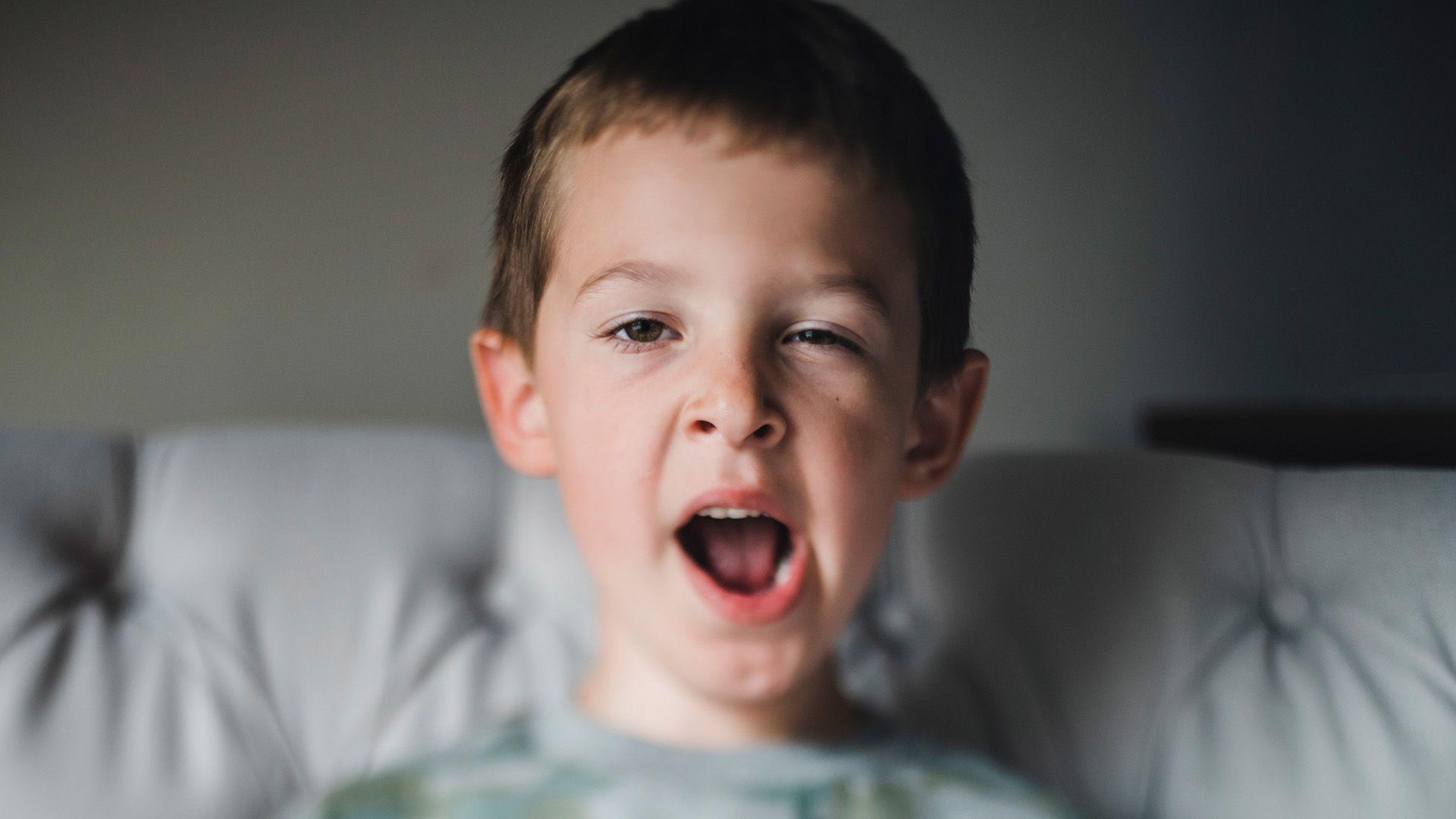 A boy sits on the sofa and yawns