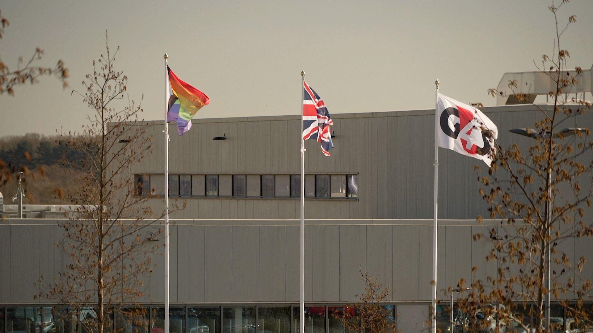Three flags flying outside HMP Five Wells; the LGBTQ+ flag; the Union Jack and a third bearing the G4S logo