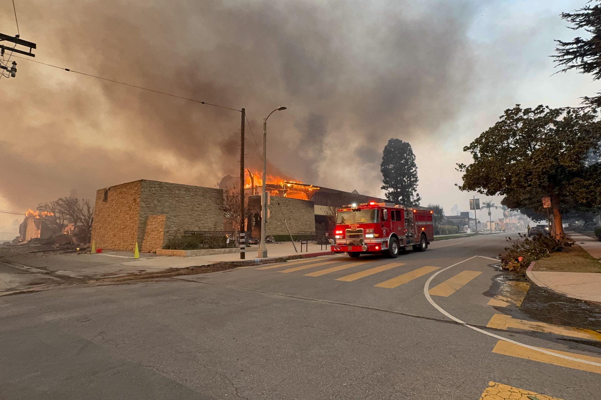 A fire engine drives down Sunset Boulevard as a building butns in the background with smoke rising on Wednesday