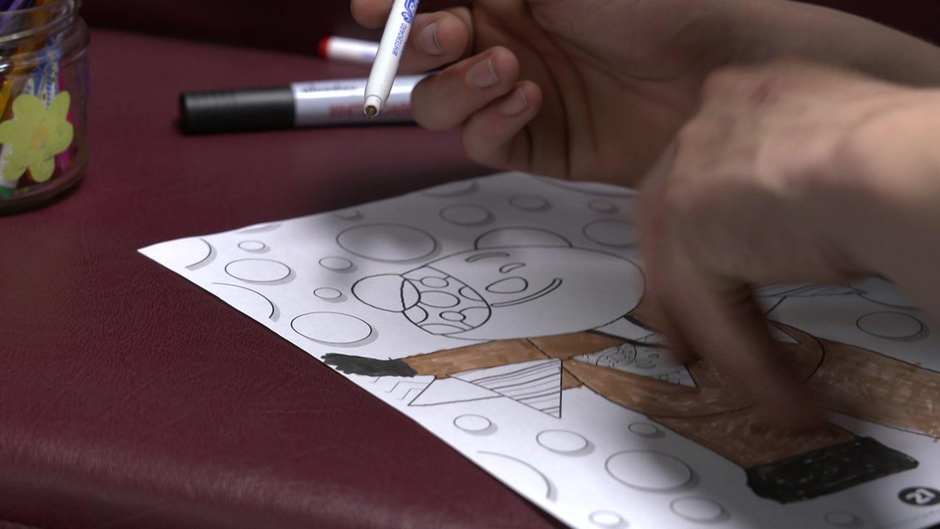 A pair of hands colouring in a Pudsey the bear mascot with a polka dot eye patch.