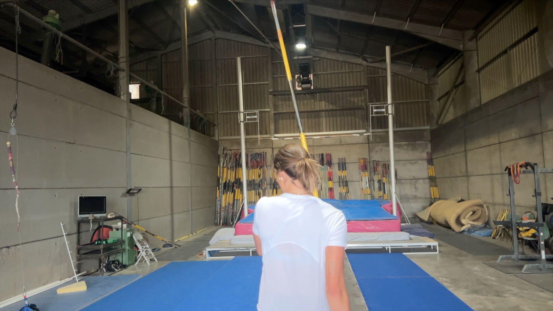 Gemma Tutton, wearing a white athletics vest and carrying a pole, runs towards a vaulting bar.