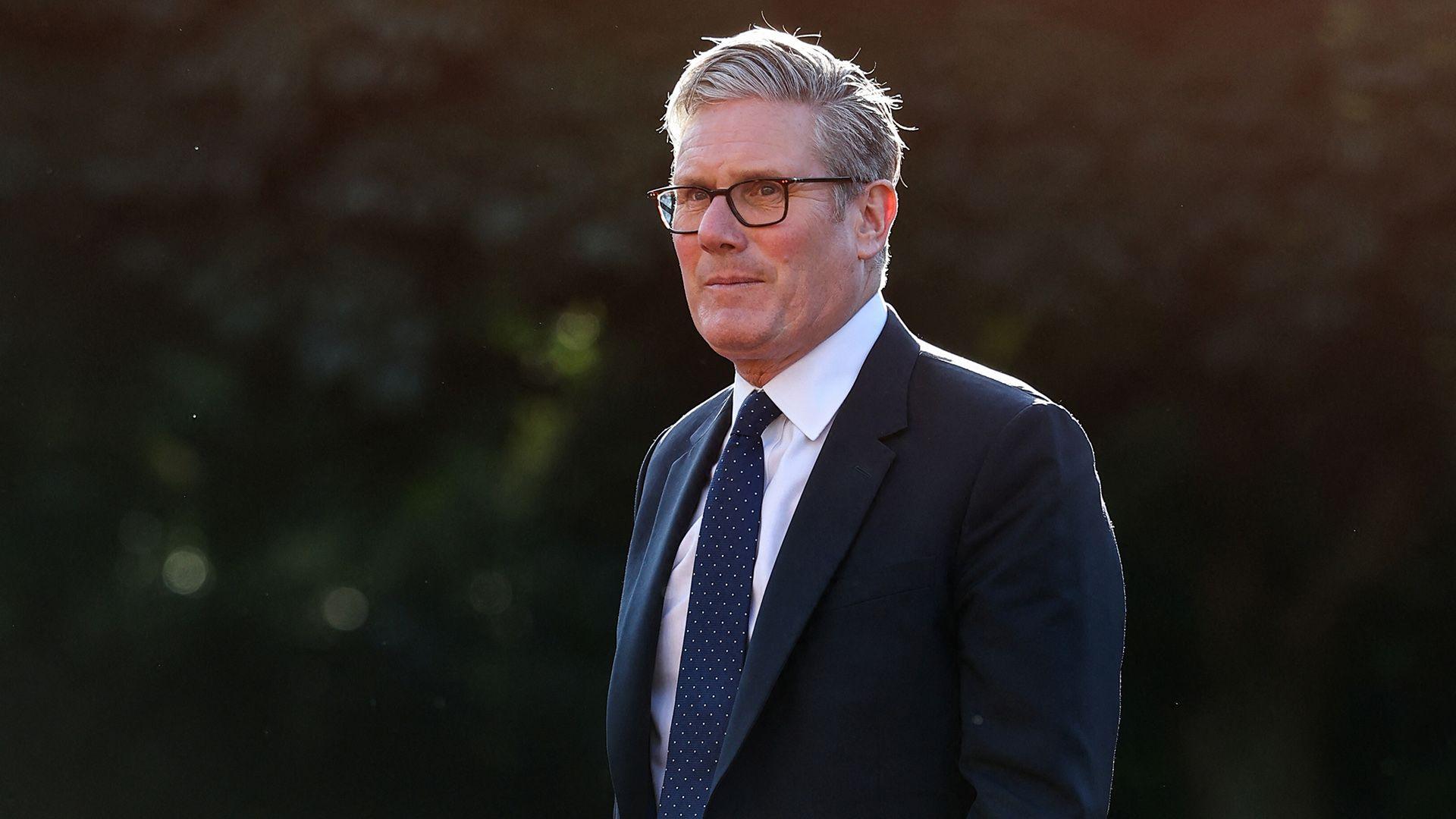 Keir Starmer looks away from camera while wearing a suit and tie and glasses against a dark background as he walks while attending the Nato summit in The Hague on 24 June