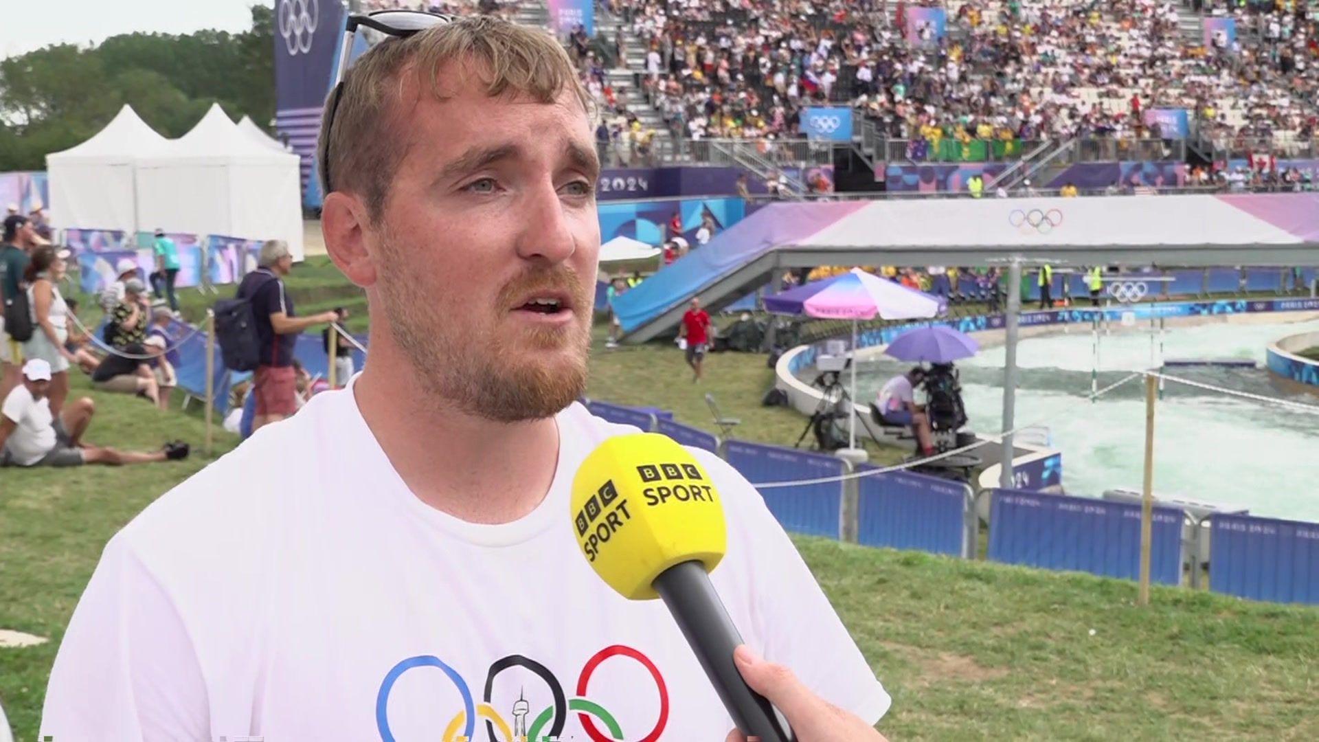 Ciaran Edwards wearing a white Olympics T-shirt stood in front of a BBC Sport microphone at the watersports centre in Paris 