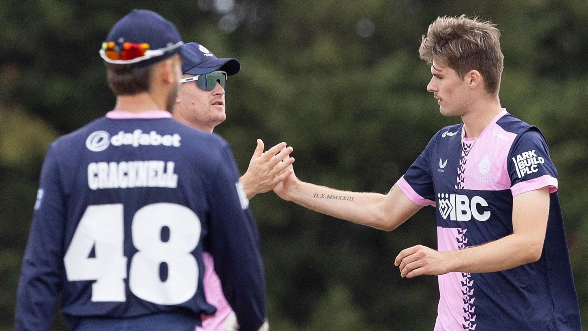 Middlesex players in blue and pink kits celebrate with high fives