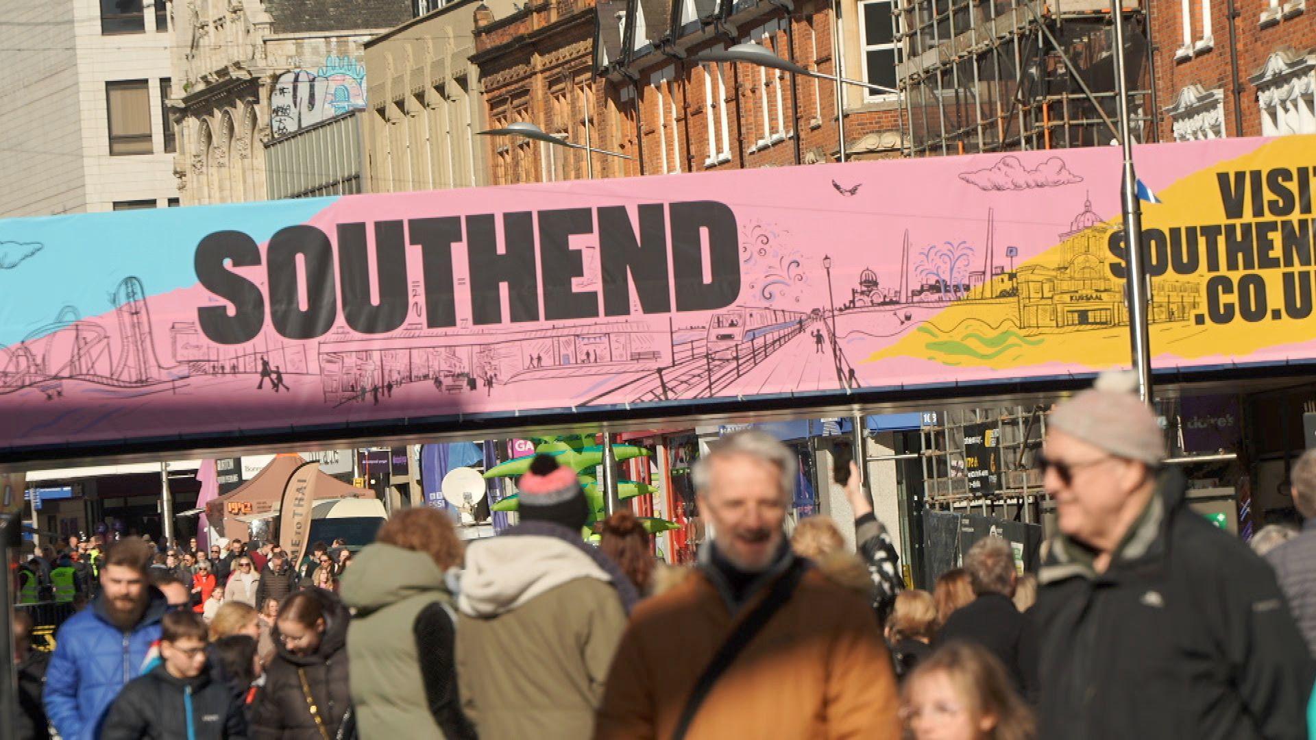 Hundreds of people milling about together in the street with a large banner saying Southend above them.