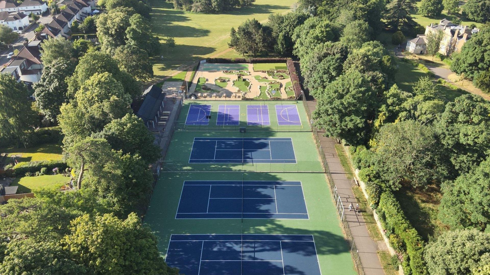 A drone view of Bury Knowle Park on a sunny day. The tennis court is visible, as well as the mini gold area.