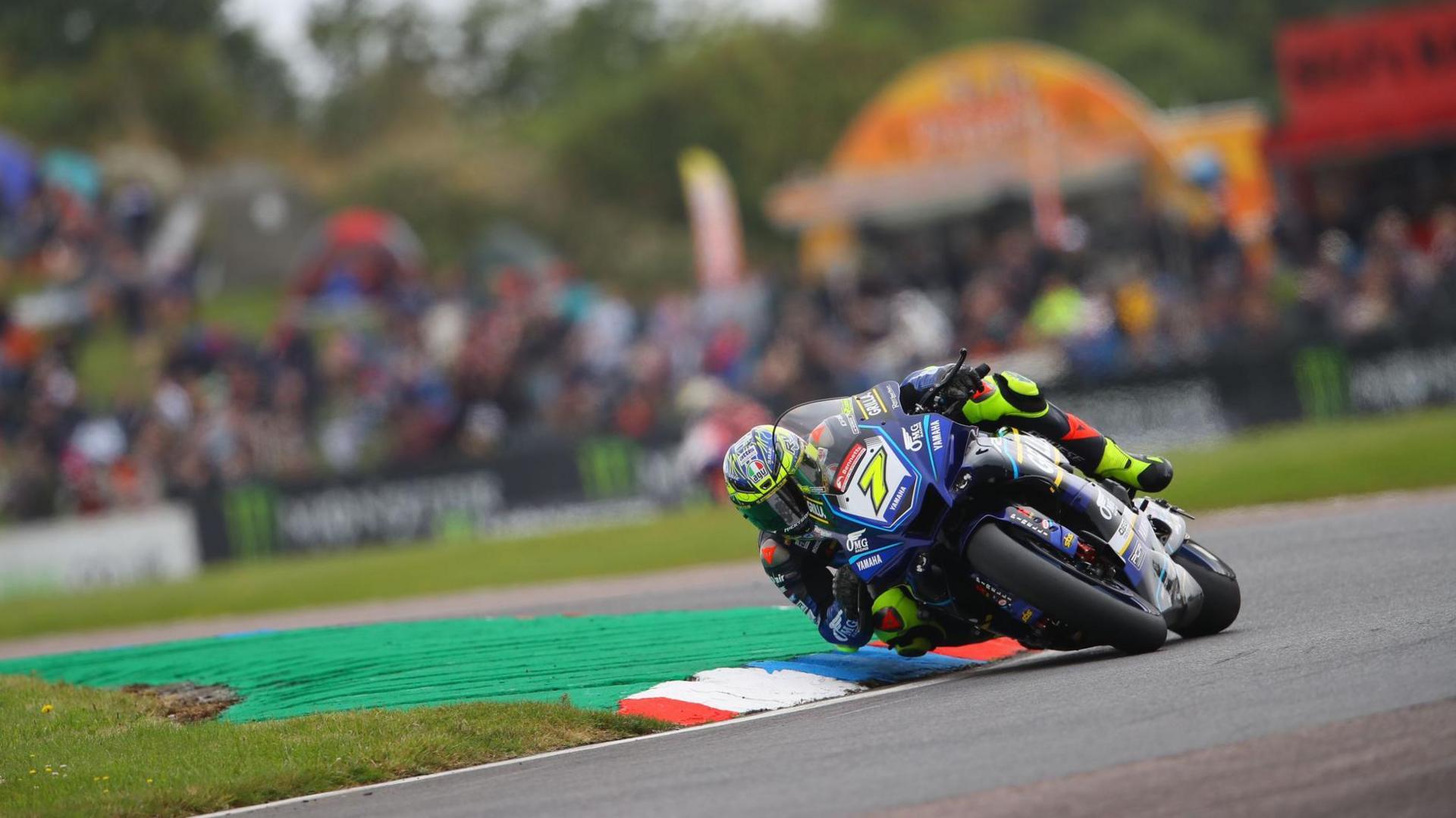 Ryan Vickers on his bike competing at Thruxton circuit, turning a bend, wearing his full kit and a helmet