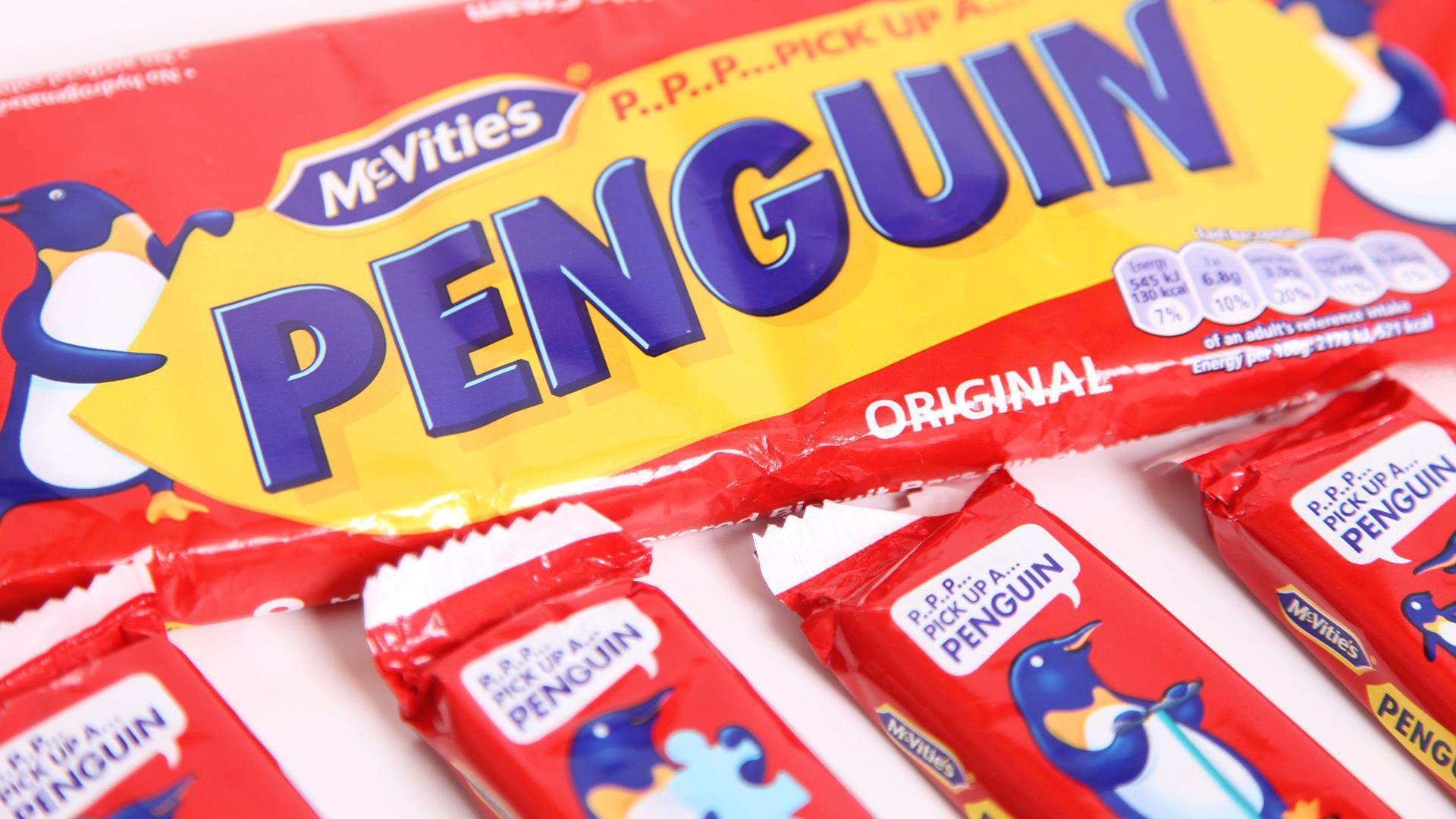 A large wrapper/packaging with the word 'PENGUIN' displayed in large blue letters. The McVitie's logo appears in the top left corner. Below the main pack are four individually wrapped biscuits, each featuring illustrations of a cartoon penguin holding a puzzle piece or other objects, above this there are speech bubbles with 'P.P.P... PICK UP A... PENGUIN' written in blue text.