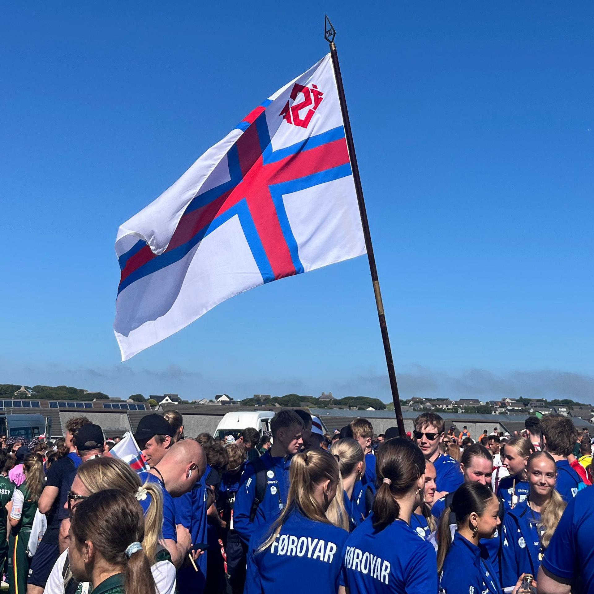 The Faroe Islands flag blowing in the wind, surrounded by athletes