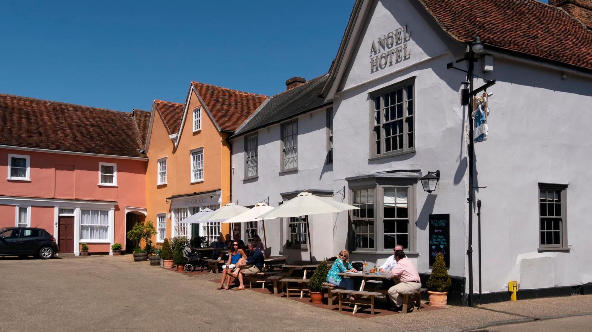 An image of the outside of the Angel Hotel, in Lavenham. People can be seen sitting outside it on tables. 