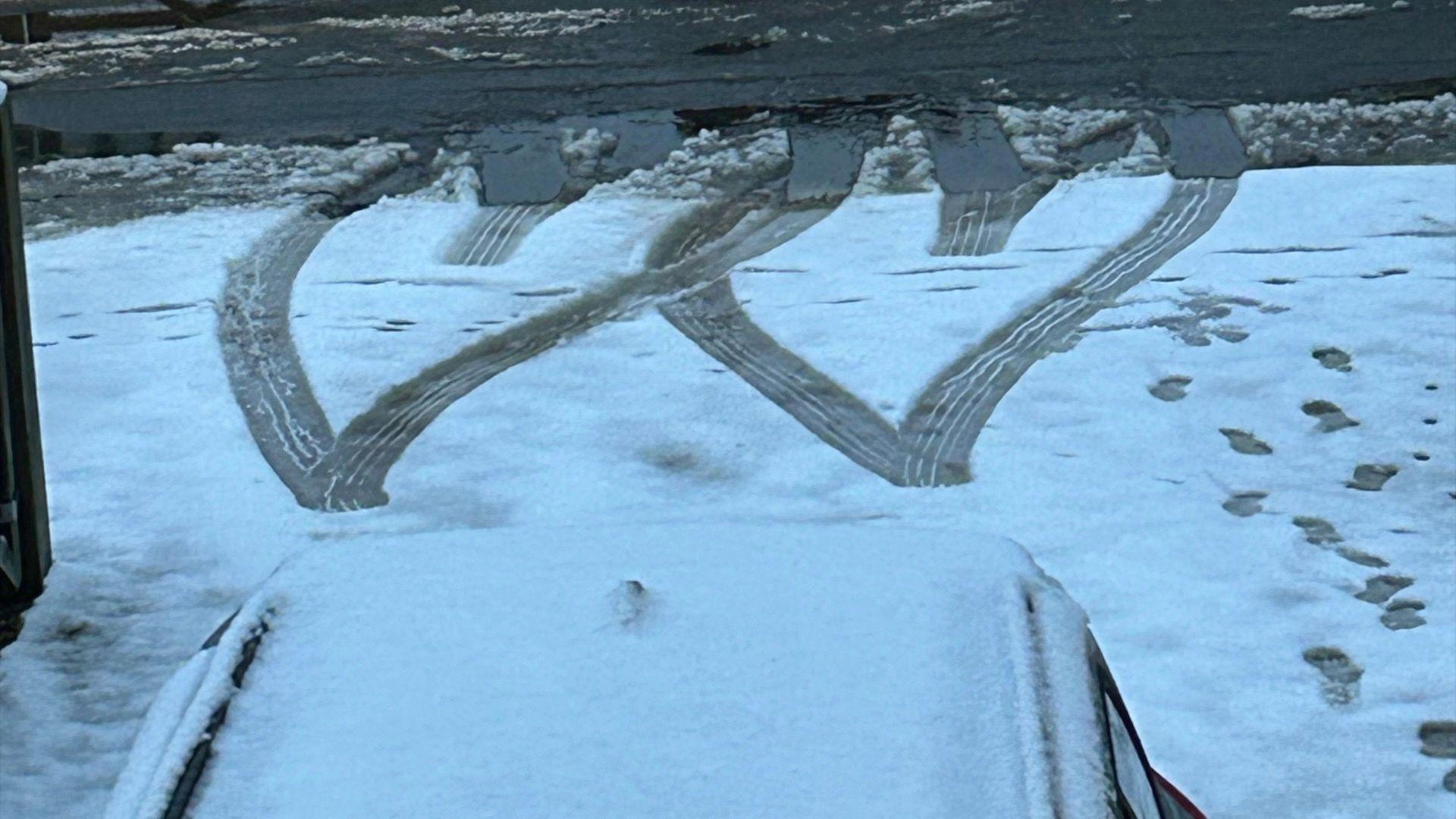 Snow ground with two hearts drawn into the ground with what looks like tyre markings. 