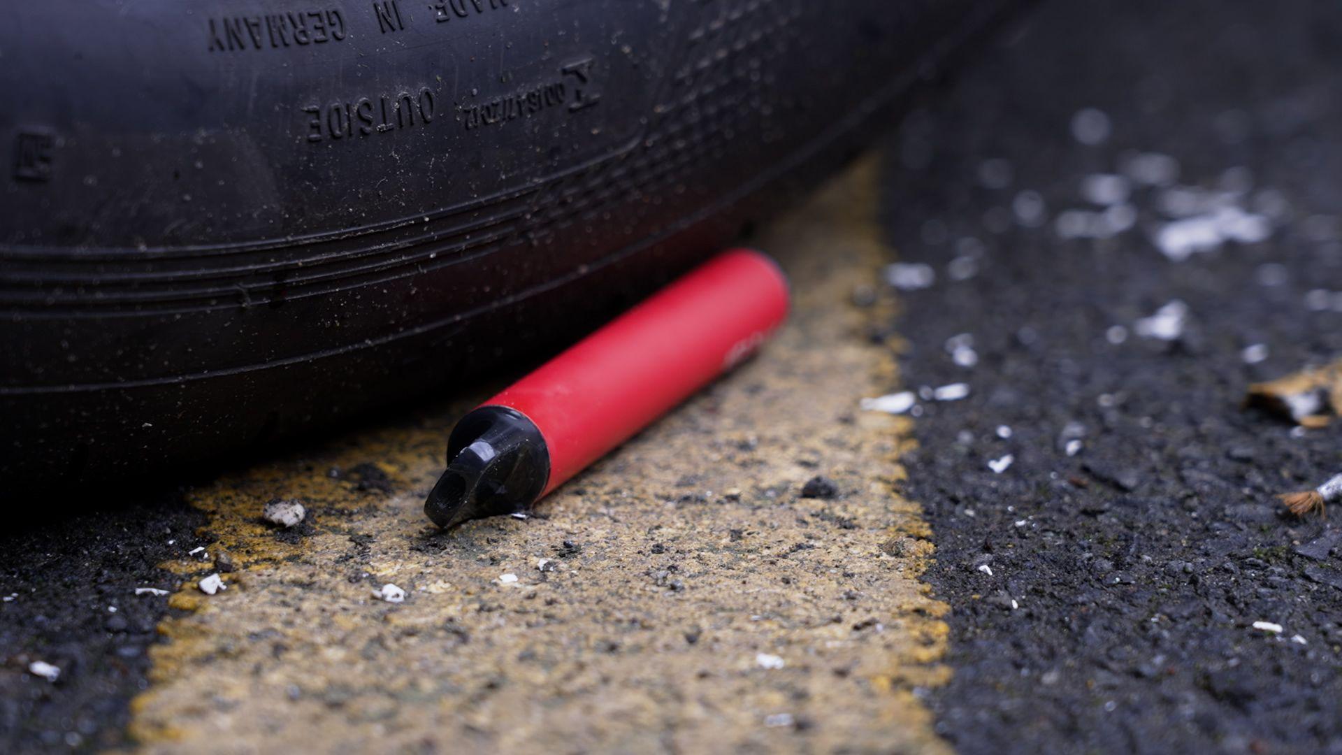 A red vape thrown away near a tyre on the road.