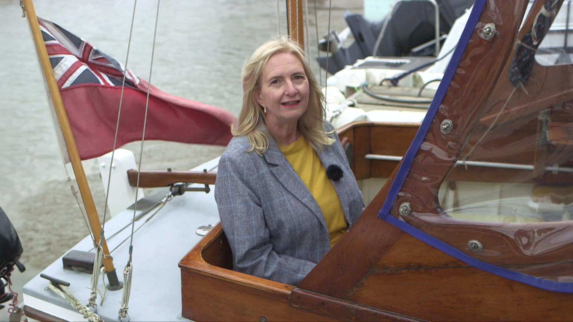 A woman with blonde hair and bright red lipstick sits in a boat.