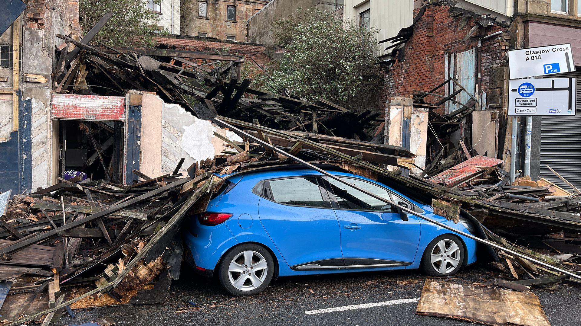 A pile of rubble on top of a blue car on a street at daylight