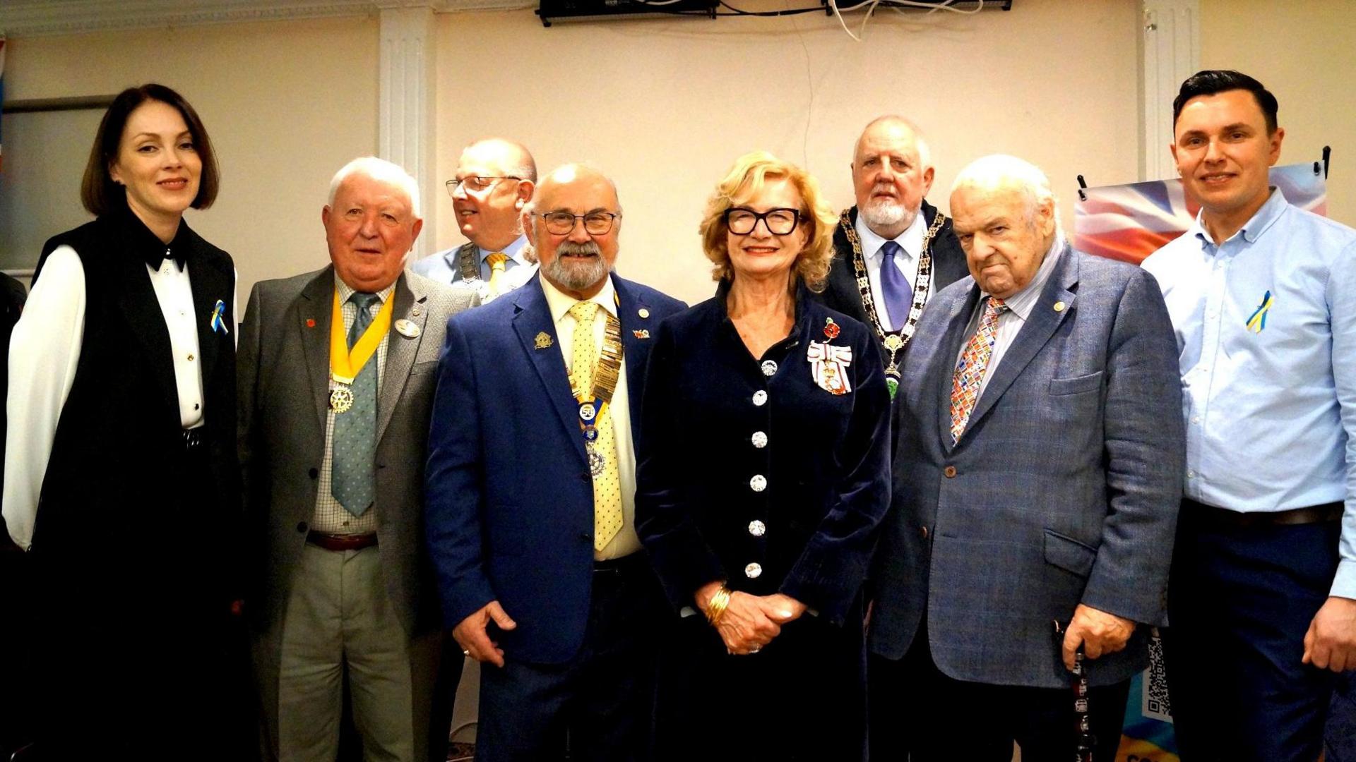 Nadia Tikhonova is furthest on the left wearing black and white. She is standing with a group or Rotarians who are all dressed in smart attire.