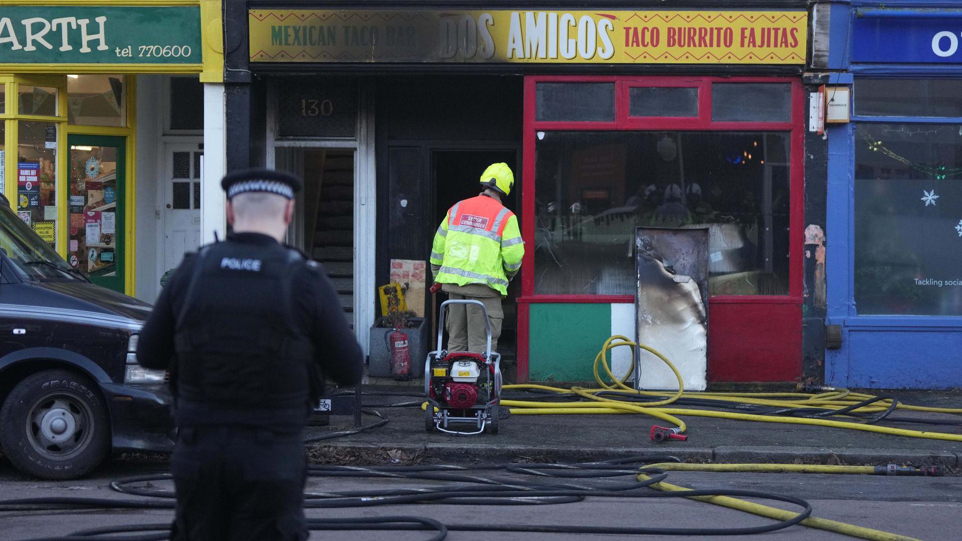 A firefighter peers into a burnt restaurant front.