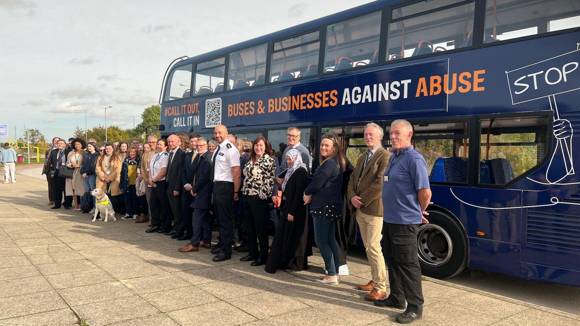 A group of people standing in front a bus sign-written with a "buses against abuse" sign.