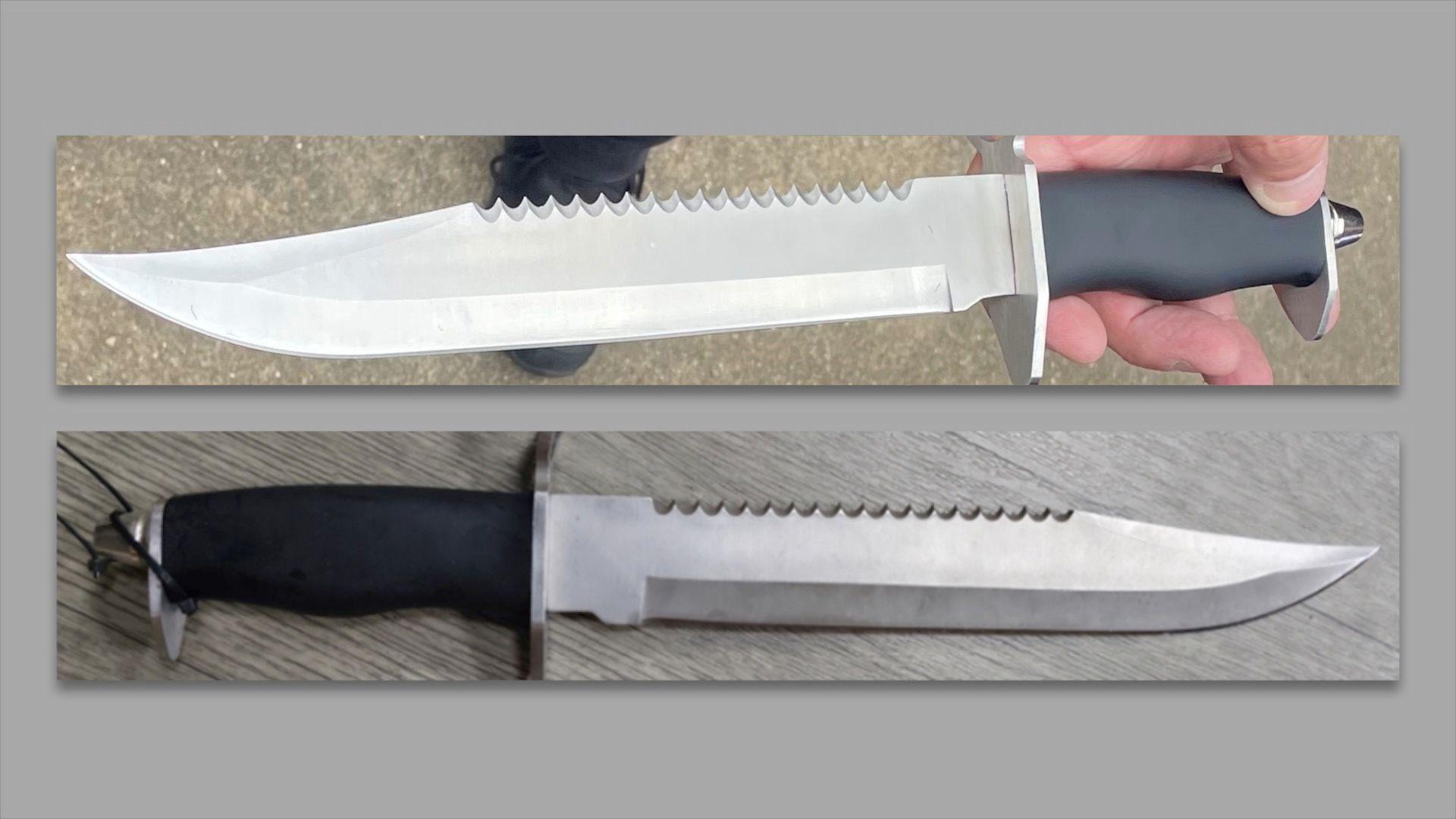 Two identical-looking bayonet-style hunting knives. They have blades that are sharpened on one side and serrated on the other and both come to a sweeping point. They both appear to have rubber or plastic handles. One is being held by a hand, while the other is lying on a light grey surface. 