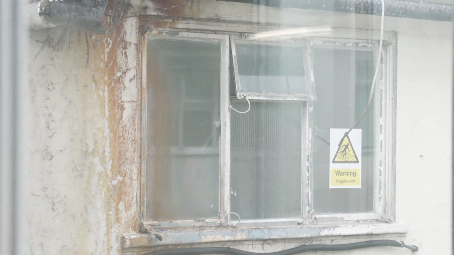 A very old, broken hospital window, with a sign saying "Warning, fragile roof"