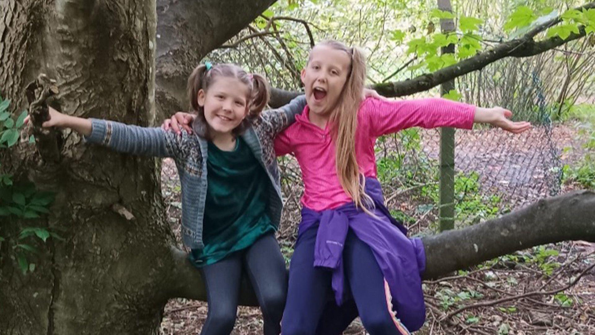 Bryanna (R) and her brother Lucian smiling and sitting on a branch of a tree with their arms around each other.