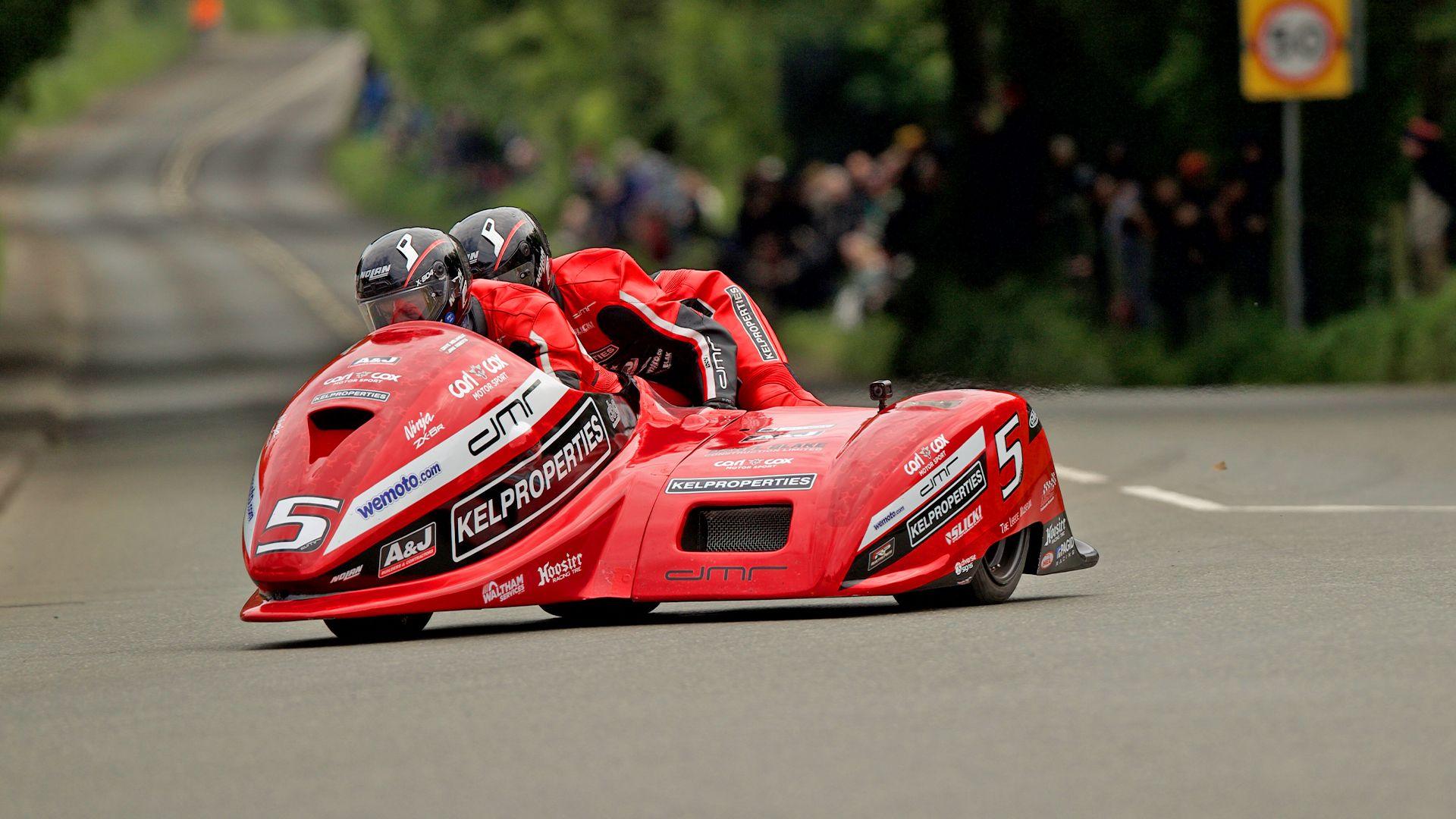 A bright red sidecar outfit on race track with crowds and greenery in the background