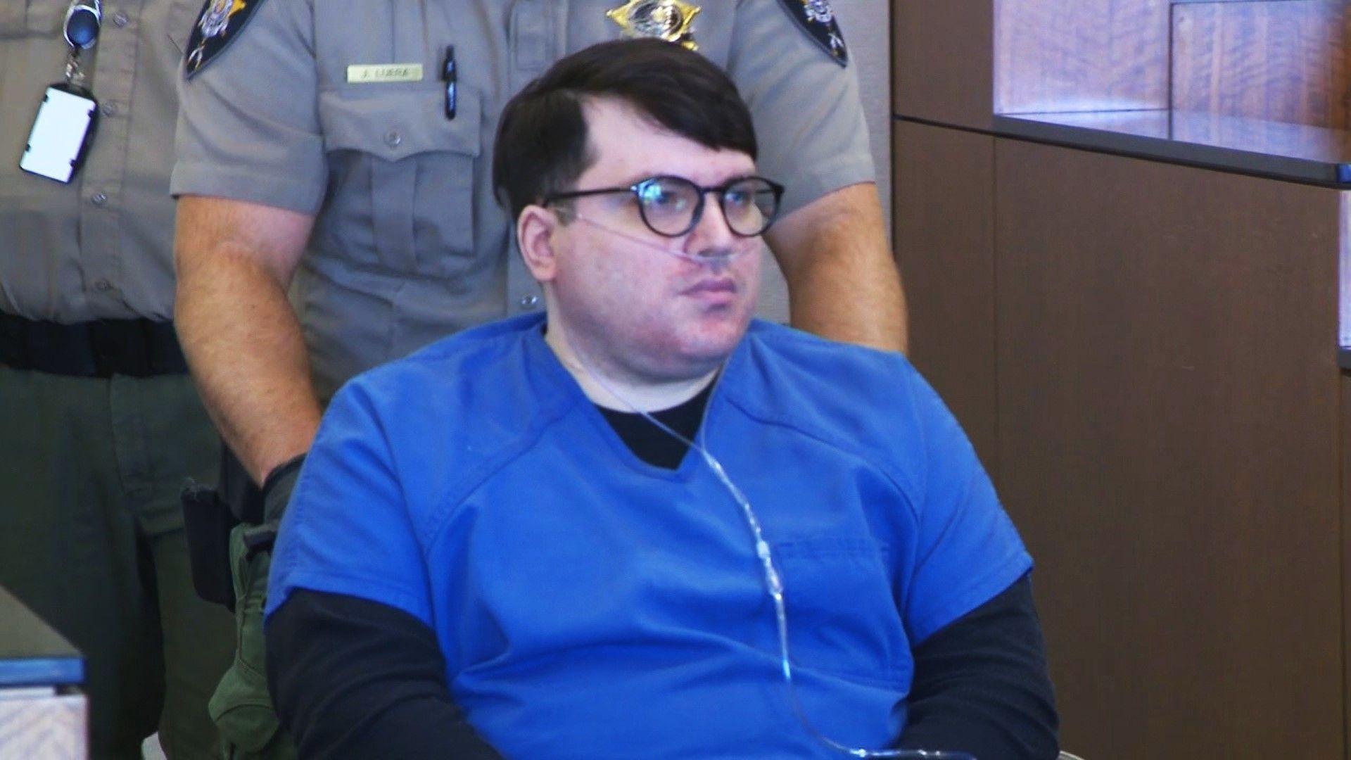 Nicholas Ross is brought into the Utah courtroom in a wheelchair. He is wearing a blue prison uniform and has an oxygen tube connected to his nose