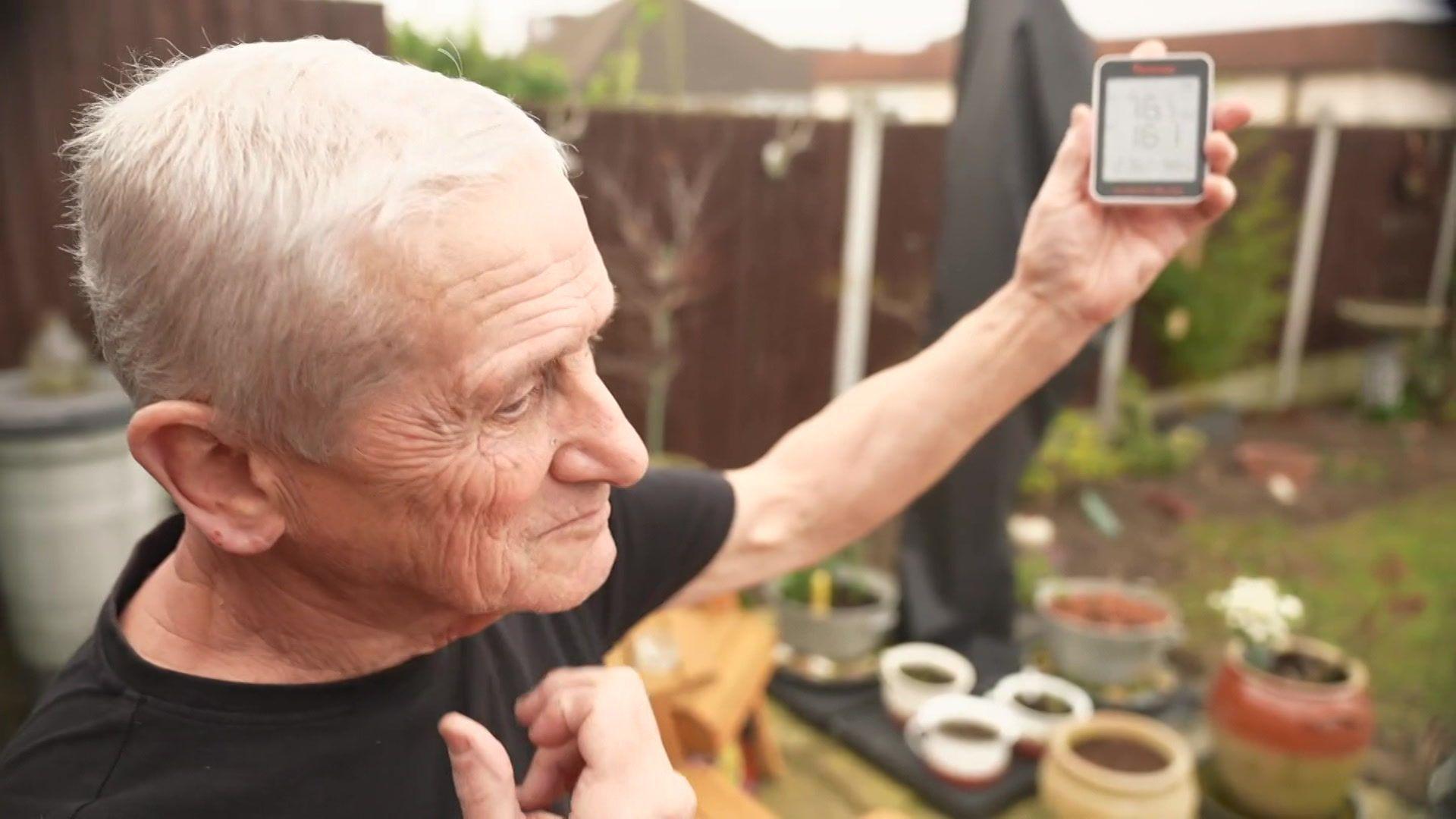 An elderly man holds up an air monitoring device in a back garden