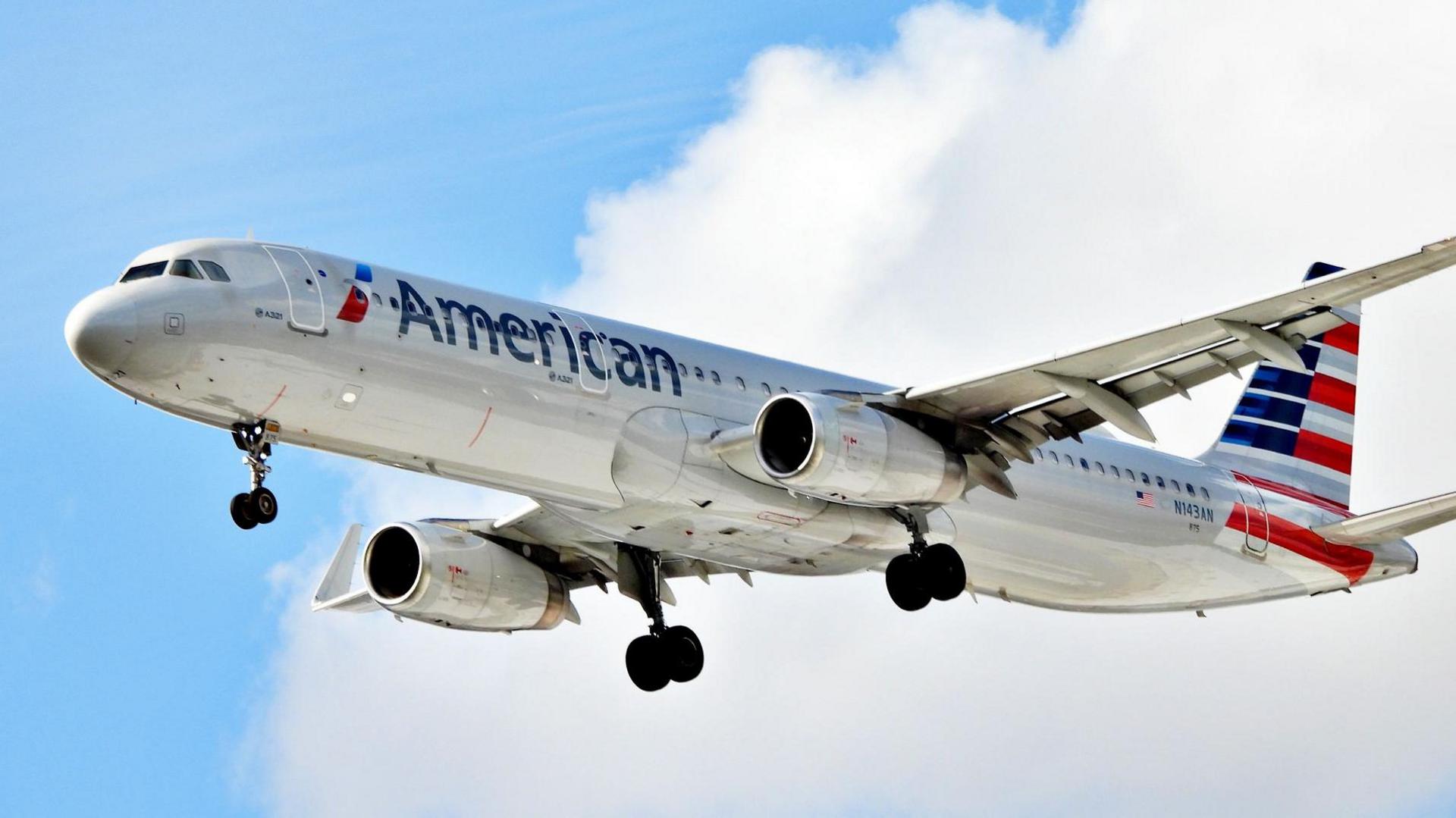 An American Airlines flight in mid-air, with the stars and stripes flag on its tail