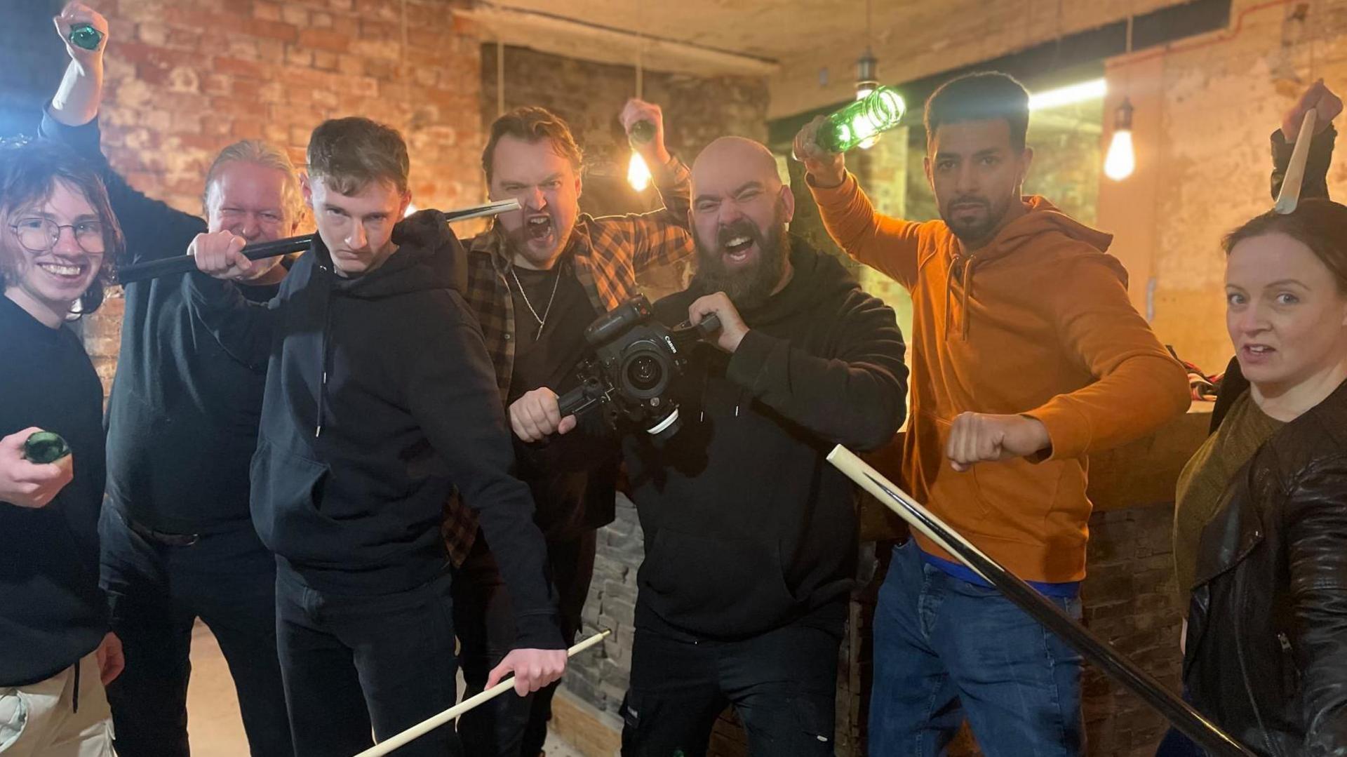 A gang of men and women holding a variety of weapons including broken bottles and snooker cues pose for the camera