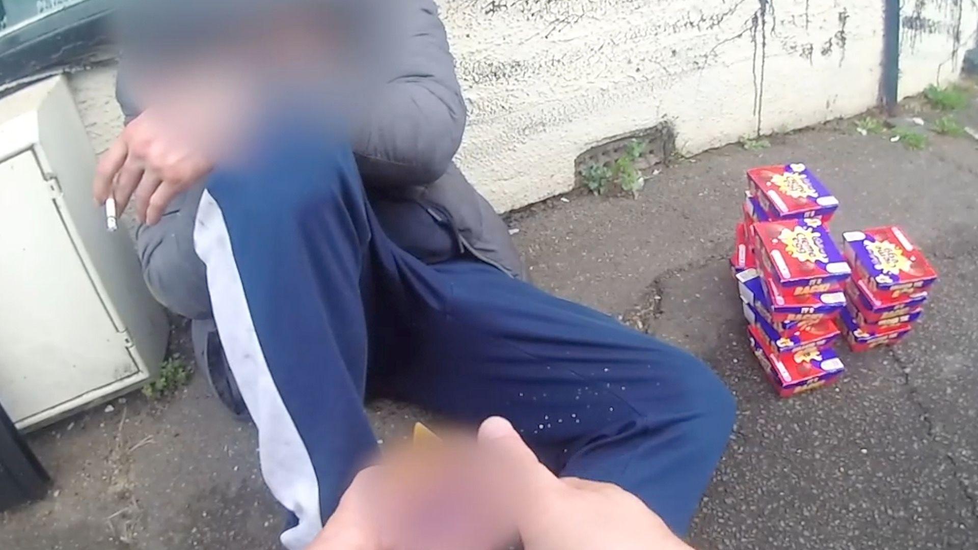 A man sat on a pavement with a pile of Cadbury Creme Eggs next to him