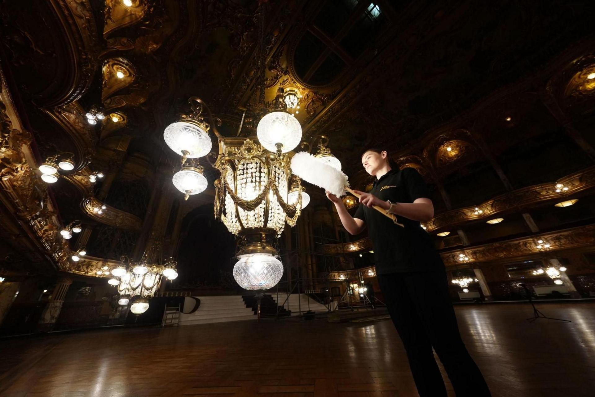 A woman cleans a chandelier with a feather duster in the Blackpool Tower Ballroom