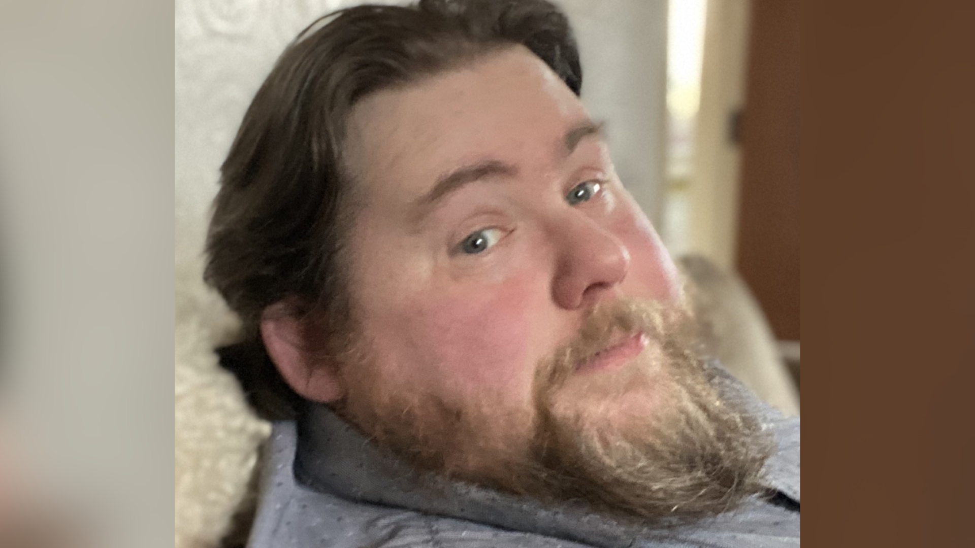 A man with dark hair and a beard looks at the camera to his side.