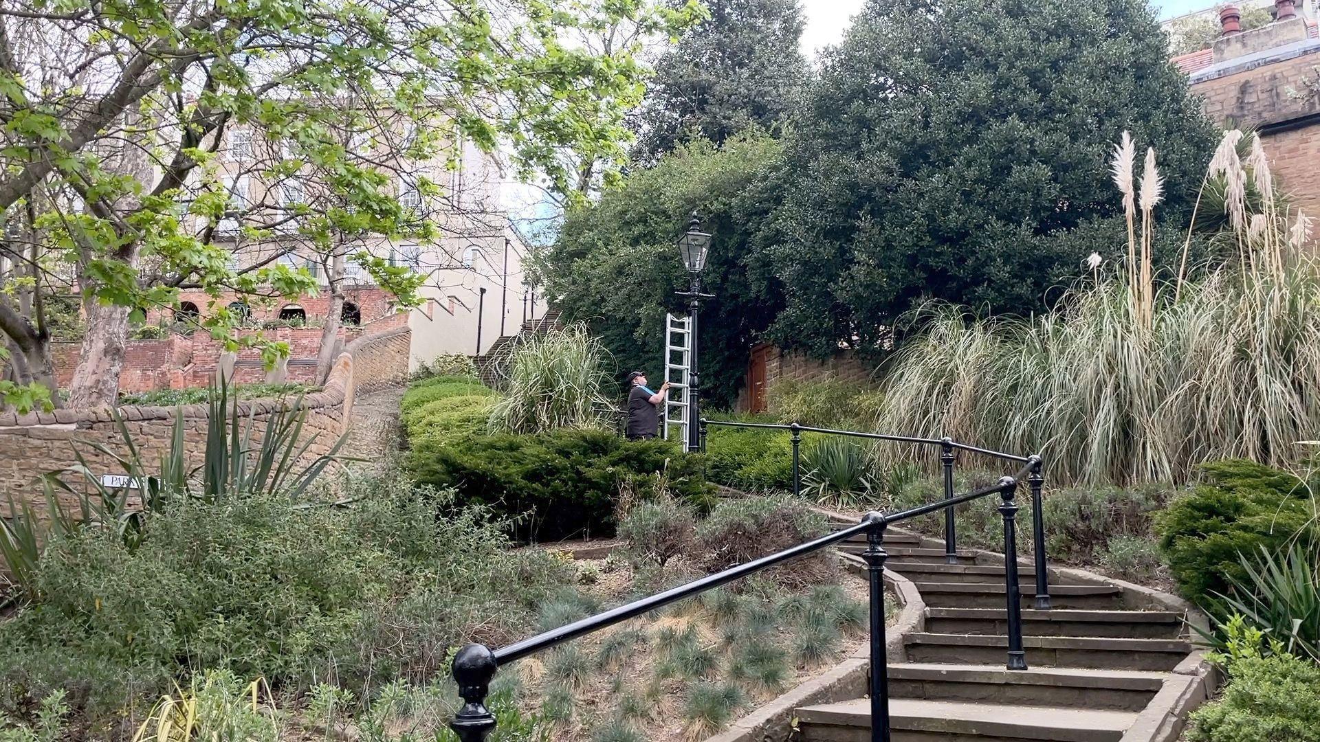 Ryan Stanton holds a ladder next to a gas lamp as he prepares to climb up