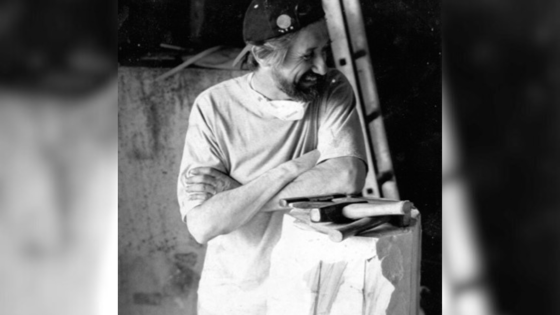 Paul Mason resting on an unfinished sculpture, with tools next to him