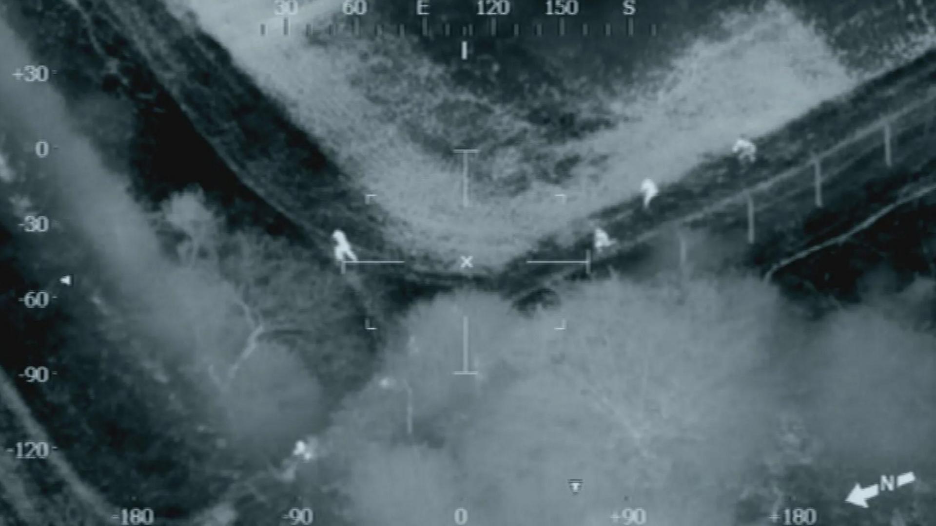 Heat-detecting footage from a helicopter shows a group of men splitting up as they run through a field.