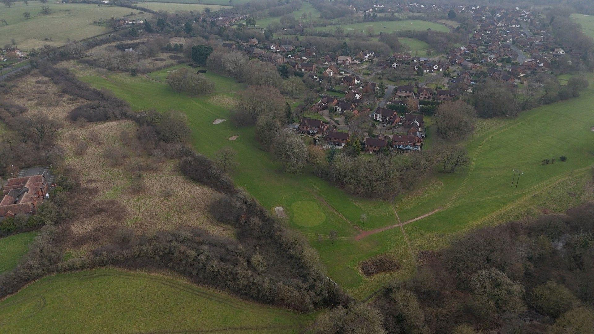 An aerial photography shows the area of the Abbey golf course that would be developed, as well as partially-wooded scrubland to the west. The existing Hither Green Lane estate is visible. 