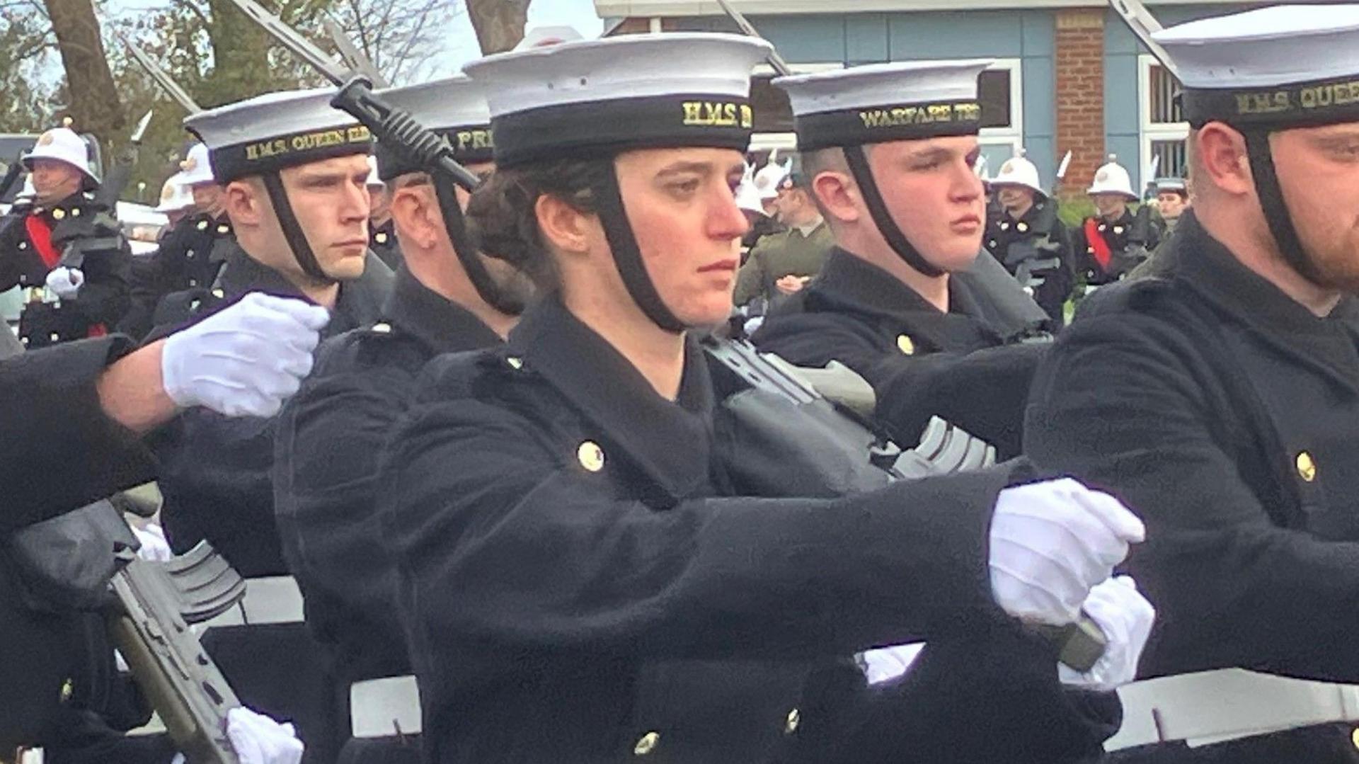 Navy personnel take part in a parade in blue uniforms and flat caps.