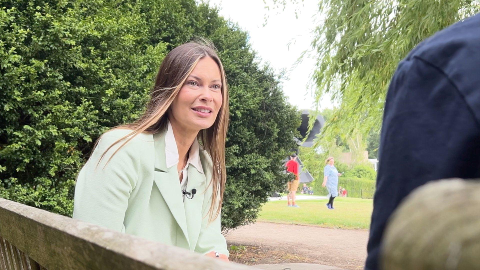 Ossett and Denby Dale MP Jade Botterill sits on a bench at the Yorkshire Sculpture Park. She has brown hair and wears a green jacket. She is talking to James Vincent, BBC Yorkshire Political Editor. His back is to camera and you can only see his arm.